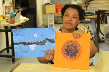 A student holding 2 paintings she made in a sensory arts class