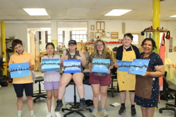 6 smiling students holding paintings they made in a sensory arts class