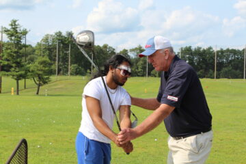 A coach teaching a student how to swing a golf club