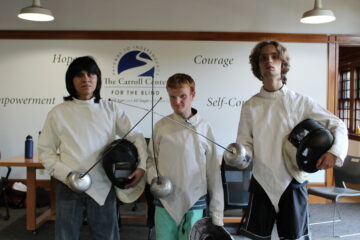 3 boys with fencing swords smiling for a group photo at the blind fencing class