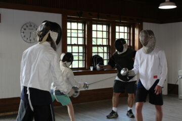 2 students fencing in pairs with instructors at the blind fencing class