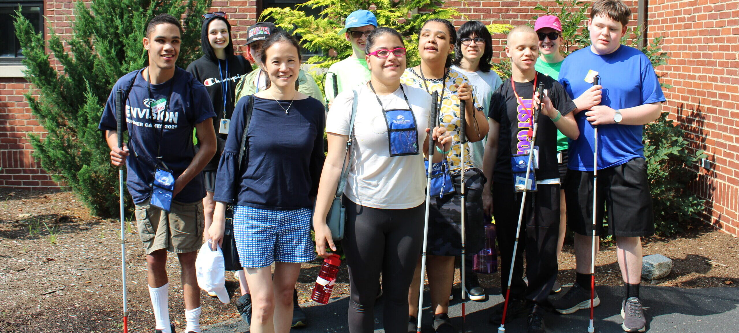 10 students with white canes smiling for a group picture with a volunteer on Field Day at the Carroll Center Newton campus