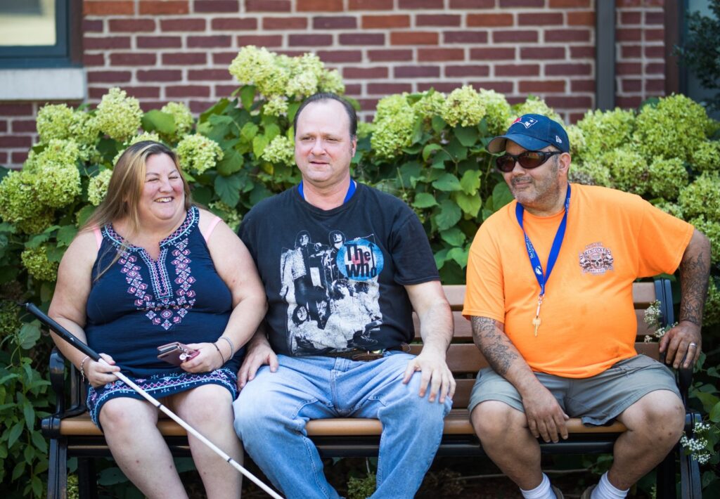 A group photo of 3 Adult Clients sitting on a bench outside