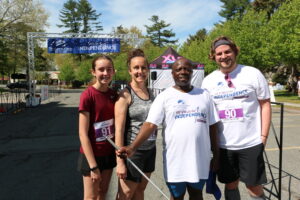 Carroll Center client standing and smiling at the Carroll Center Walk for Independence finish line with three other walk participants.