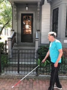 Gary is pictured walking with his white cane on the sidewalk near his home. 