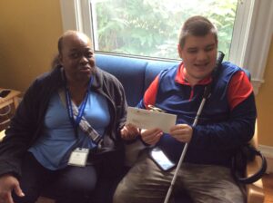 Carroll Center client, Tallen, holding his first paycheck while sitting next to his job coach, Elizabeth.