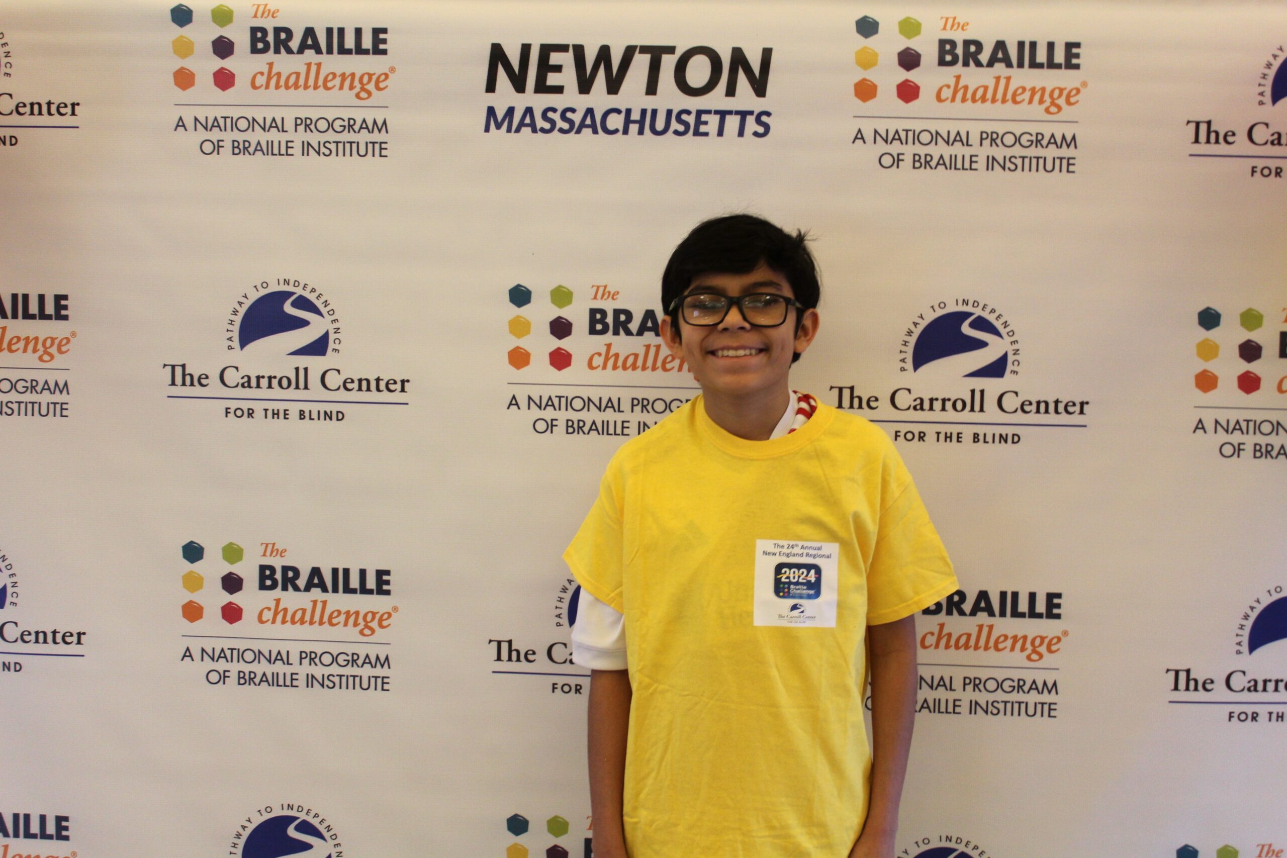 Braille Challenge participant smiling for a photo in front of the Carroll Center Braille Challenge backdrop
