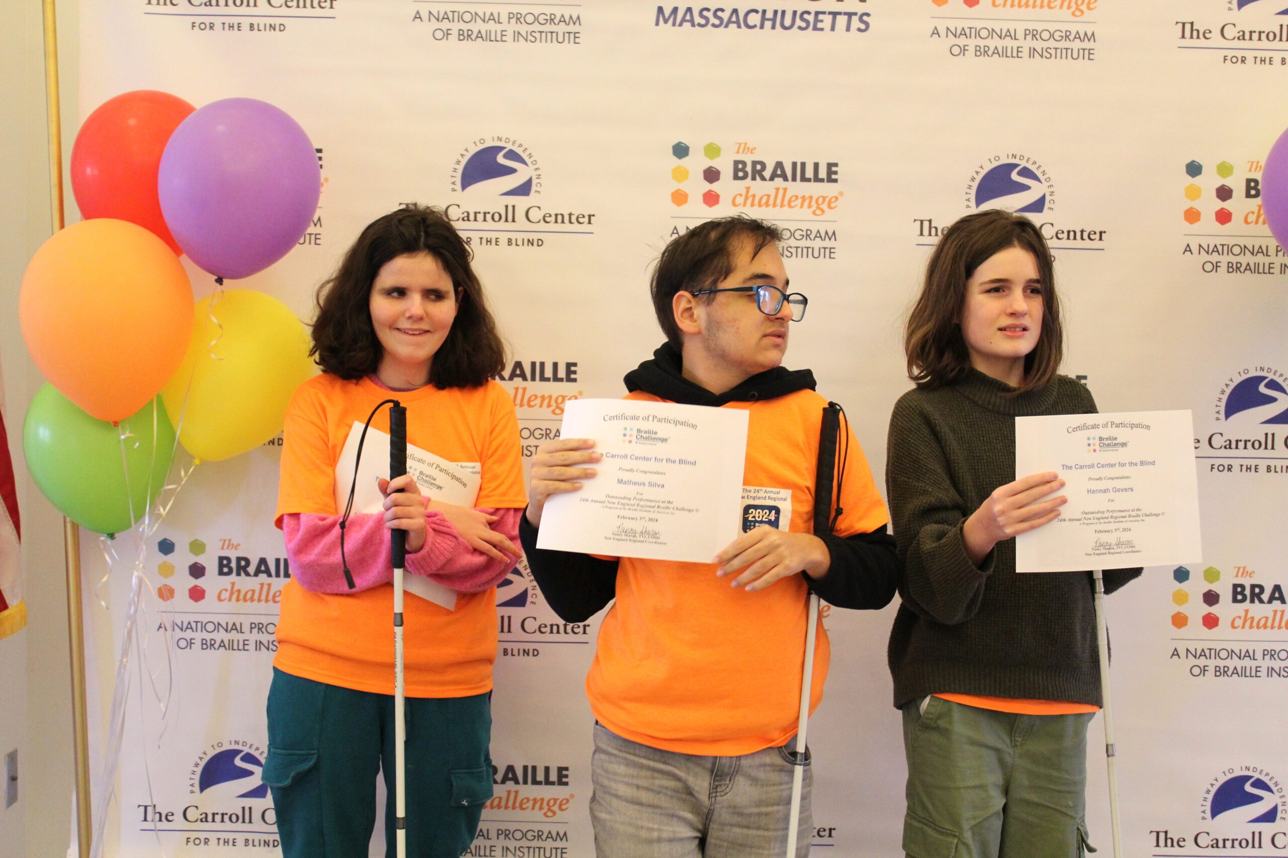 3 Braille Challenge participants smiling for a photo with certificates in front of the Carroll Center Braille Challenge backdrop