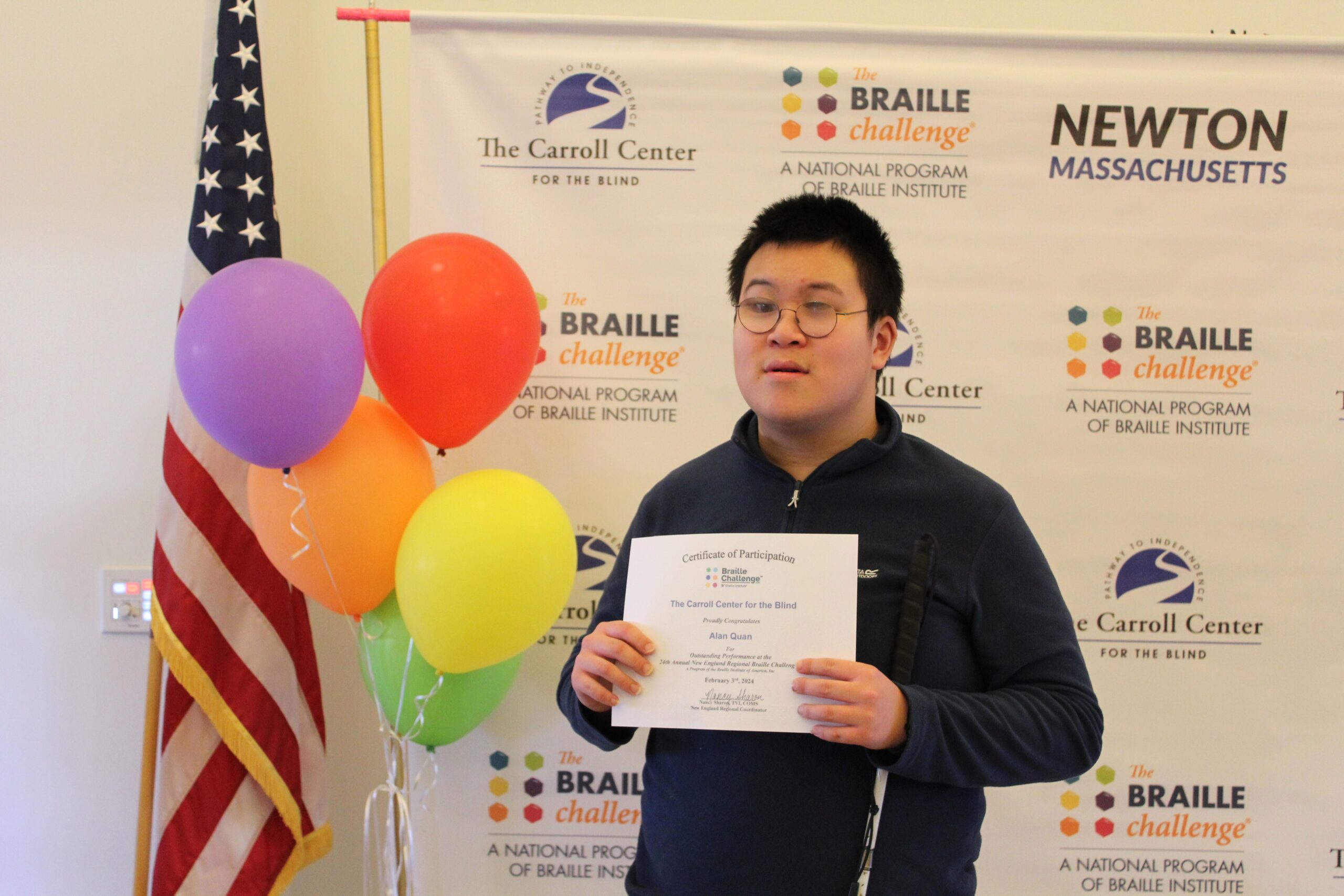 Braille Challenge participant smiling for a photo with a certificate in front of the Carroll Center Braille Challenge backdrop