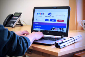 Person typing on a computer. A white cane appears on the desk suggesting the person may be visually impaired.