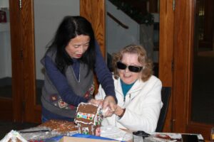 Carroll Center volunteer assisting a senior client decorate a gingerbread house during a group evening activity