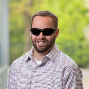 Headshot of Brian Switzer. He is a white man with short brown hair and is wearing dark glasses.