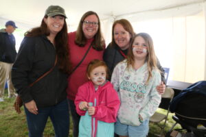 3 women and 2 young girls with face paint standing inside an outdoor event tent and smiling for a group picture.