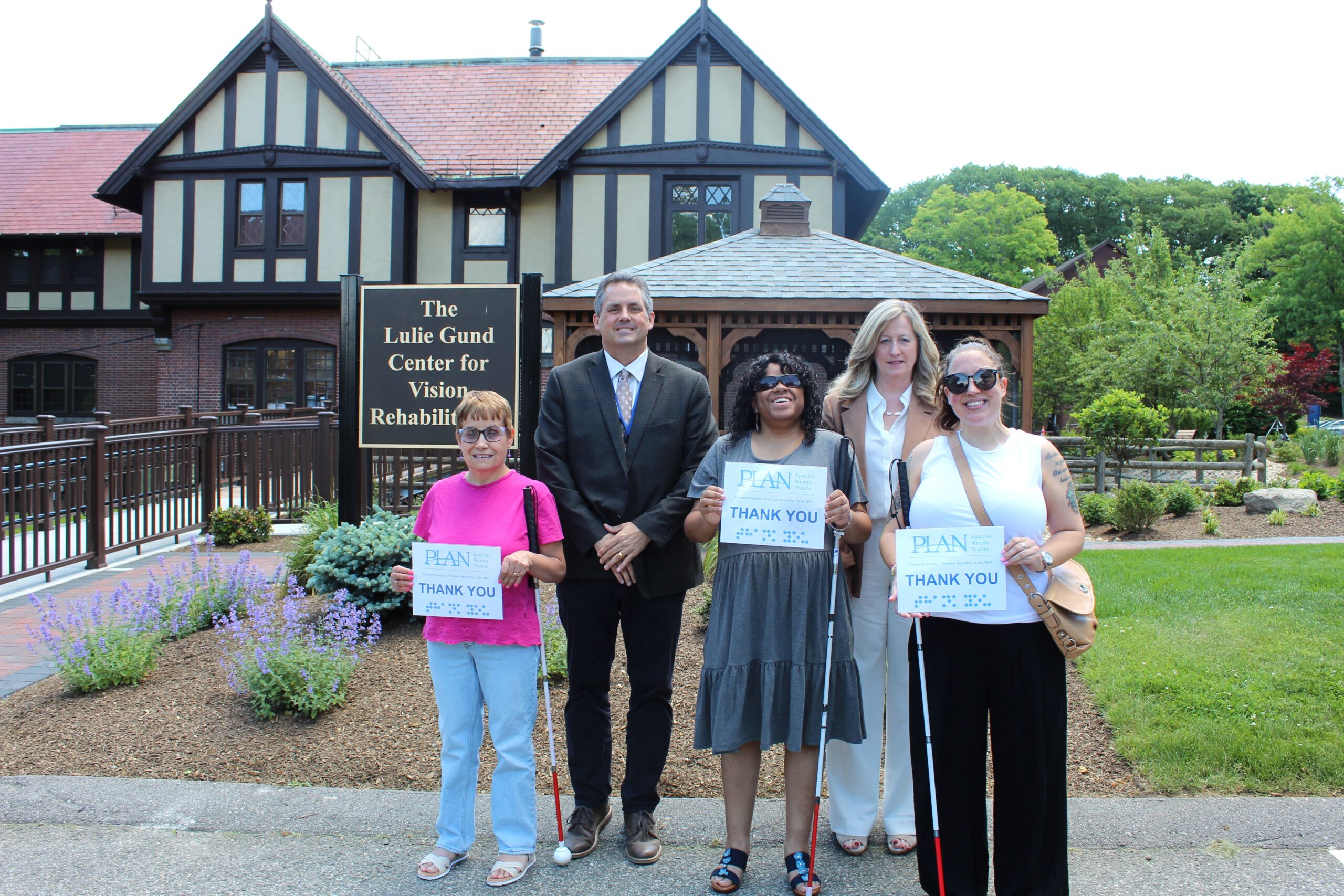 Carroll Center President and CEO, Greg Donnelly and a representative from PLAN stand in front of The Lulie Gund Center for Vision Rehabilitation next to three women with white canes who are holding “Thank You PLAN” signs.