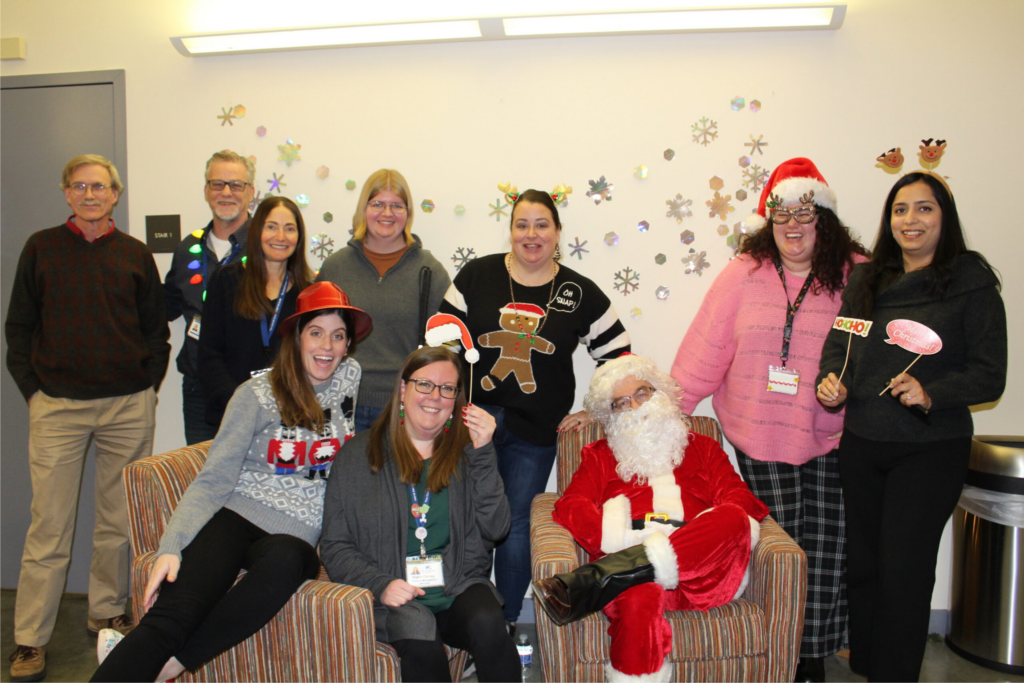 Nine Carroll Center staff members with Christmas-themed photo props posing for a photo with Santa