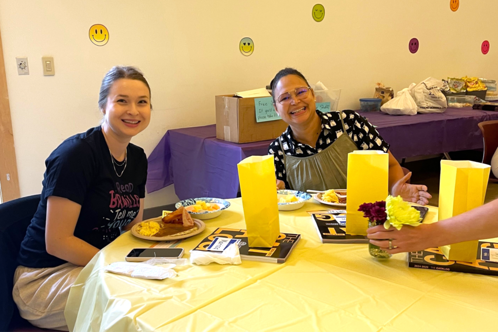 Two Carroll Center staff members sitting and smiling at a table with breakfast food