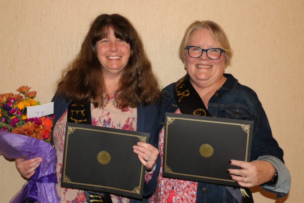 Two Carroll Center staff members smiling while holding flowers and certificates