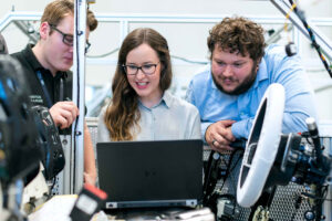 three engineers standing and talking in front of a car design model