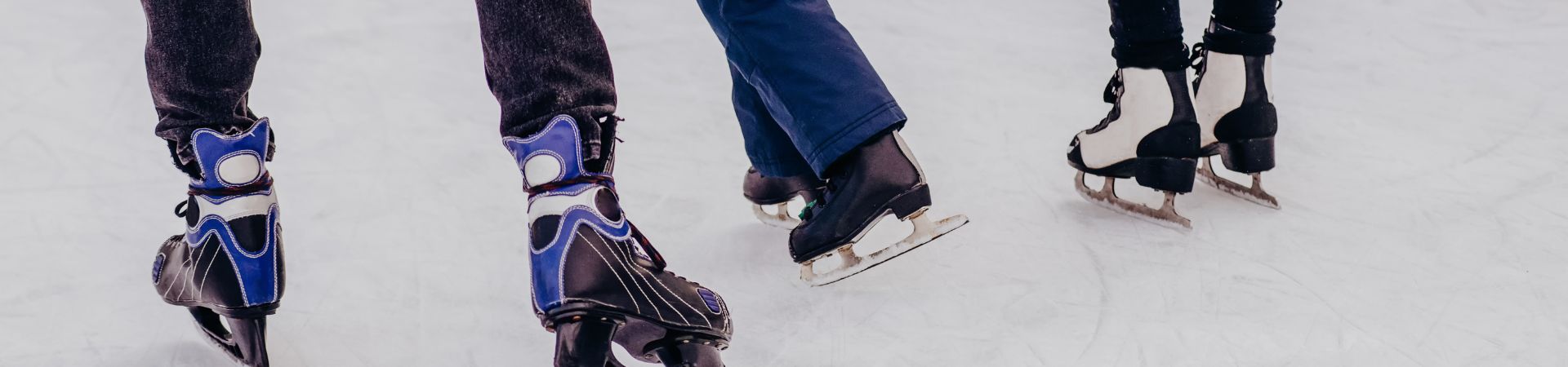 Close-up of three people's ice skates skating on the ice.