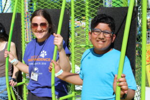 Carroll Center summer youth program student is smiling on the carnival ride with a summer program staff who is also smiling.