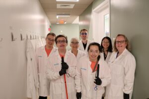 Summer students wearing white lab coats and smiling for a photo