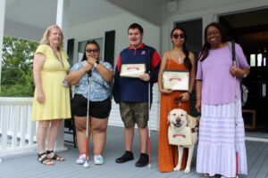 A group of Summer Program Students smiling with graduation certificates, with instructors and a guide dog by their side