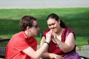 Two Summer program teens are smiling and holding hands in the park