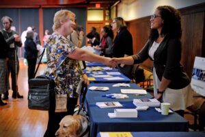 An employer is shaking hands across a table with a person with a visual impairment at a career fair.