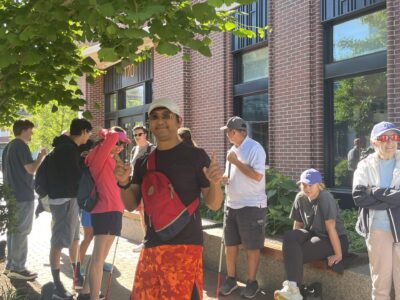 photo of volunteer, Miao, giving a "thumbs up" at the camera standing with other sailors and volunteers outside of the Whitney Hotel.