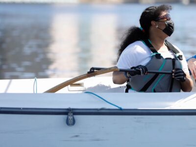 photo of sailor, Tabitha, sitting inside a sailboat holding the tiller to steer the boat.