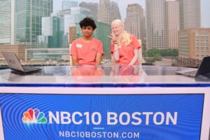 Two summer program students sit at the desk of the NBC 10 Boston station