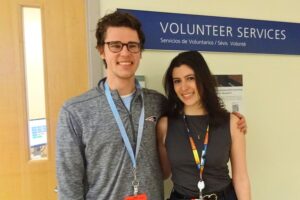 A client from the Carroll Center for the Blind stands next to an employee at the Boston Medical Center. They are infront of a sign that says "Volunteer Services".